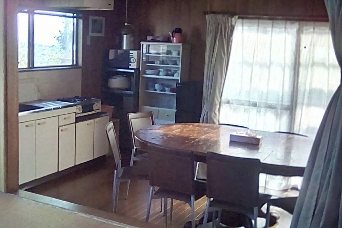 A compact kitchen with a dining table and chairs, a microwave, and a shelf with dishes.