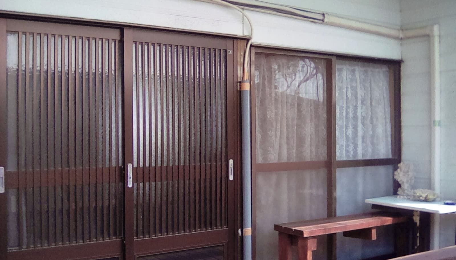 Ein Zimmer mit Schiebetür, einem kleinen Tisch und einem Fenster mit Vorhängen.
