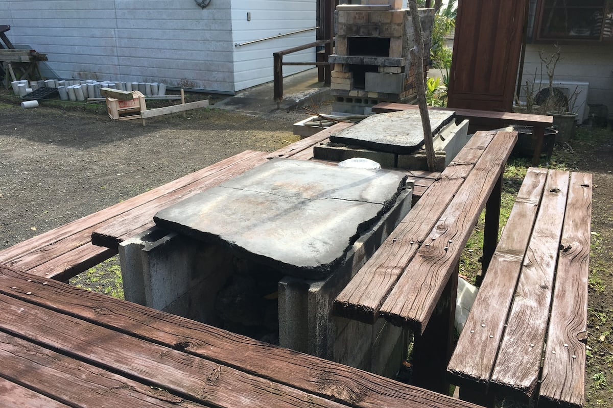 A wooden deck with a concrete slab, a brick oven, and a wooden bench.