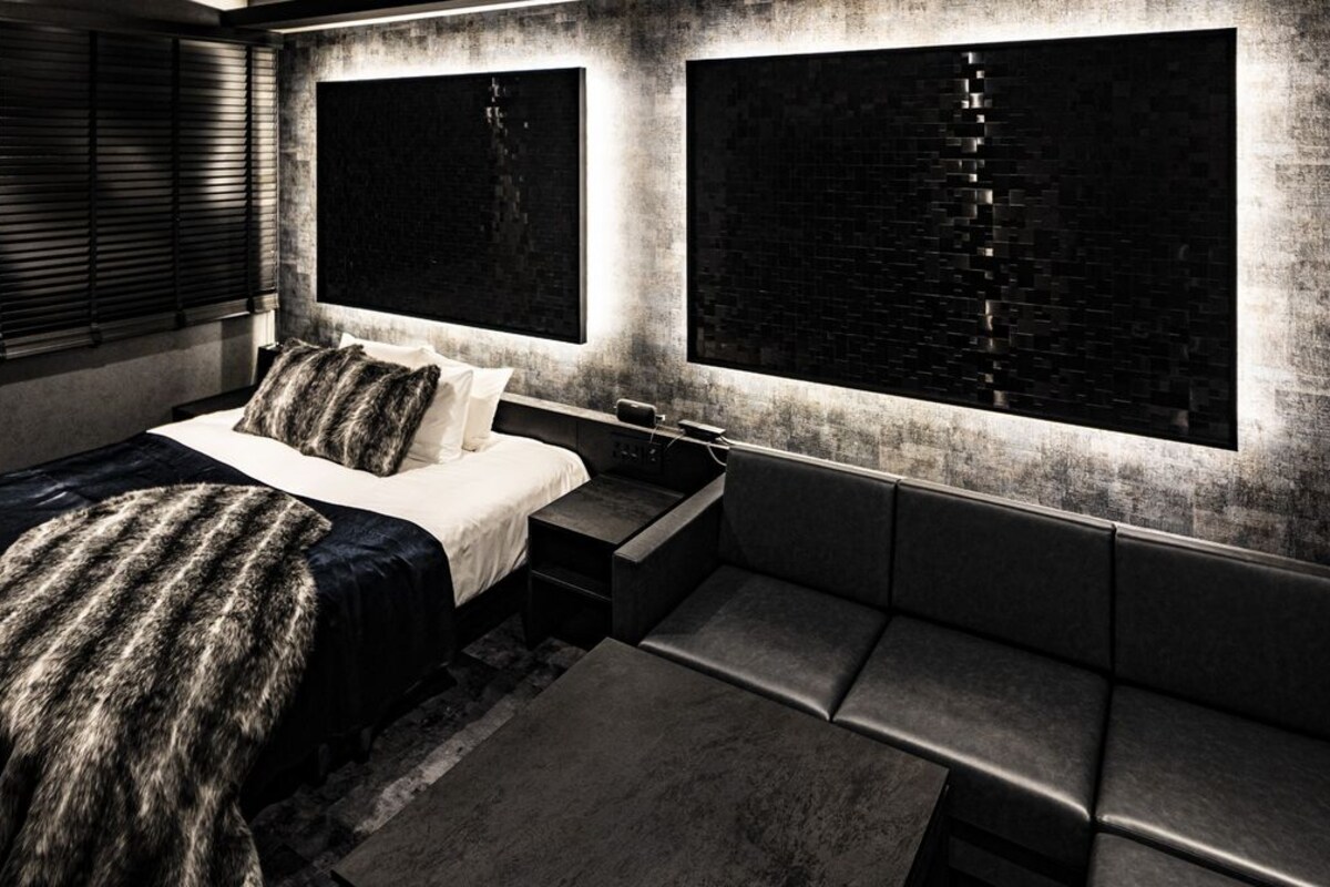 A modern bedroom with a bed, bedside tables, a bench, and large windows with blinds.
