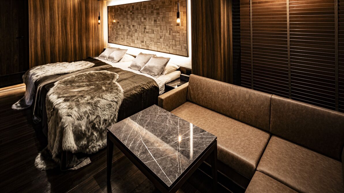 Una habitación con cama, sofá, una mesa de mármol y paneles de madera.