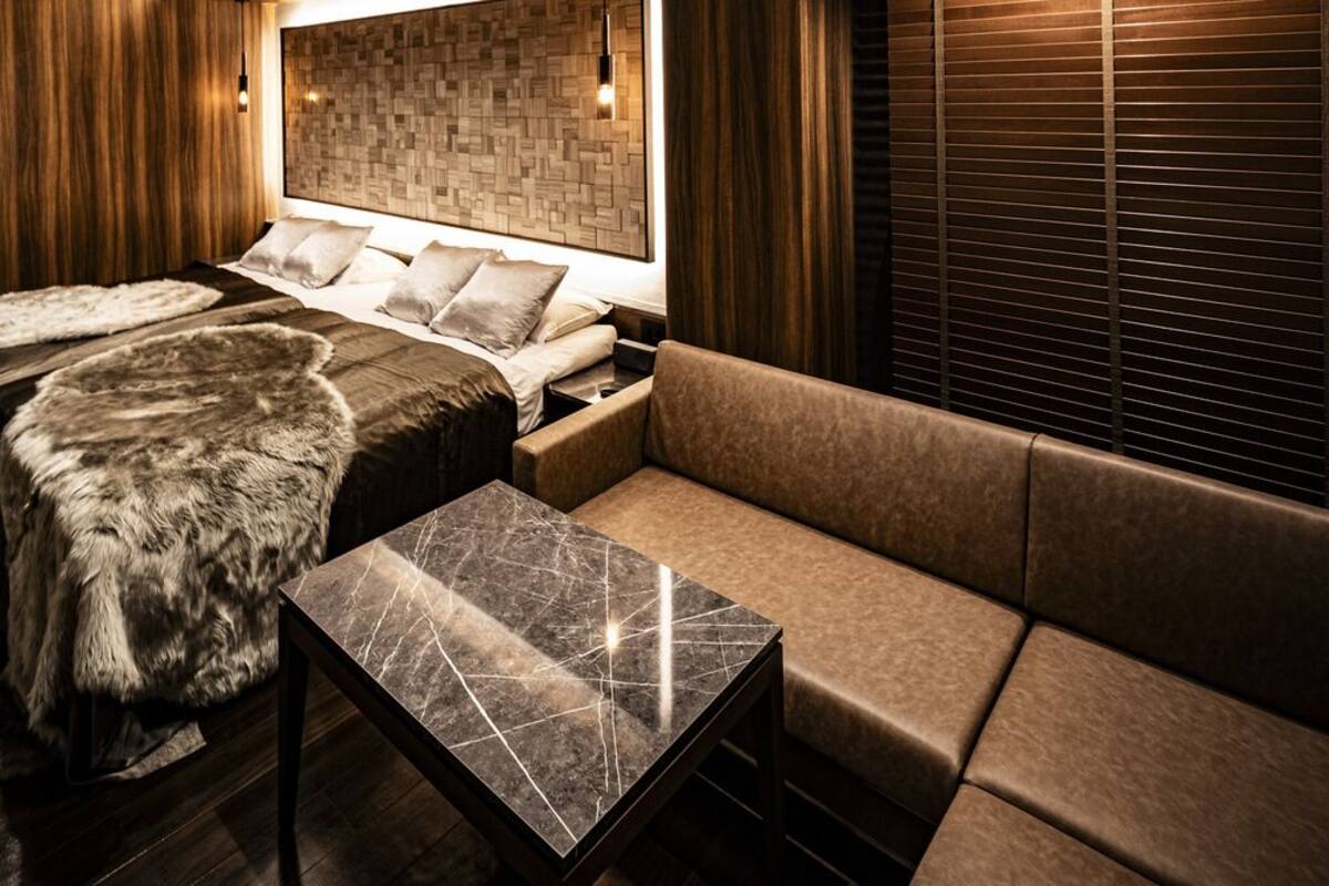 Una habitación con cama, sofá, una mesa de mármol y paneles de madera.