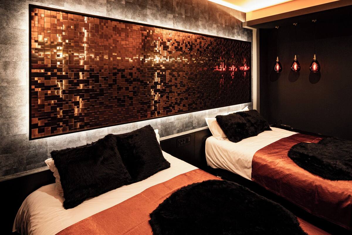 Habitación de hotel con dos camas, un panel de pared con textura e iluminación colgante.