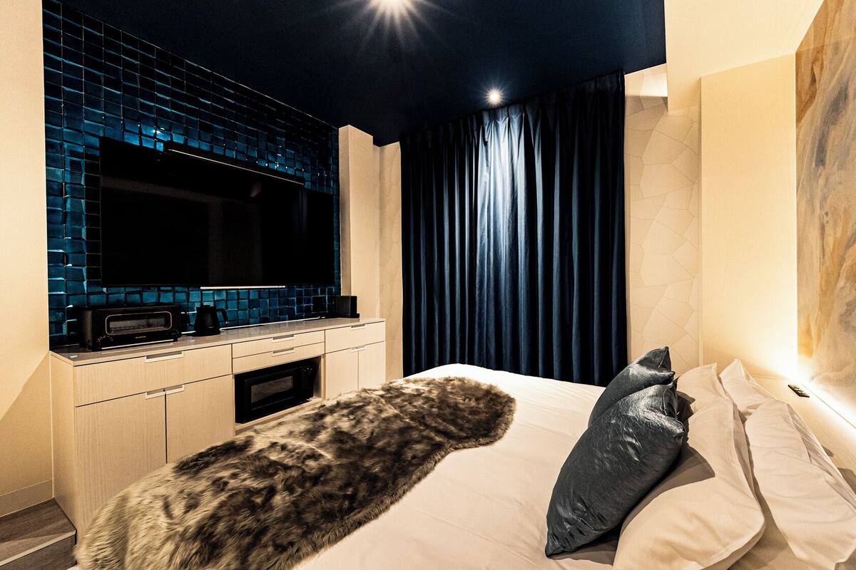 Una habitación de hotel moderna con una cama grande, televisión de pantalla plana, cocina integrada y un cuadro abstracto de gran tamaño en la pared.