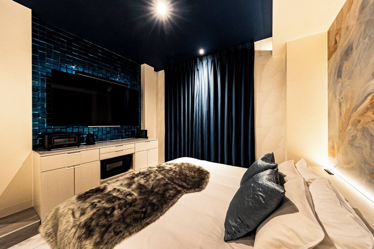 Un dormitorio moderno con una cama grande, un plaid de piel, un cuadro y una zona de cocina con salpicadero azul.