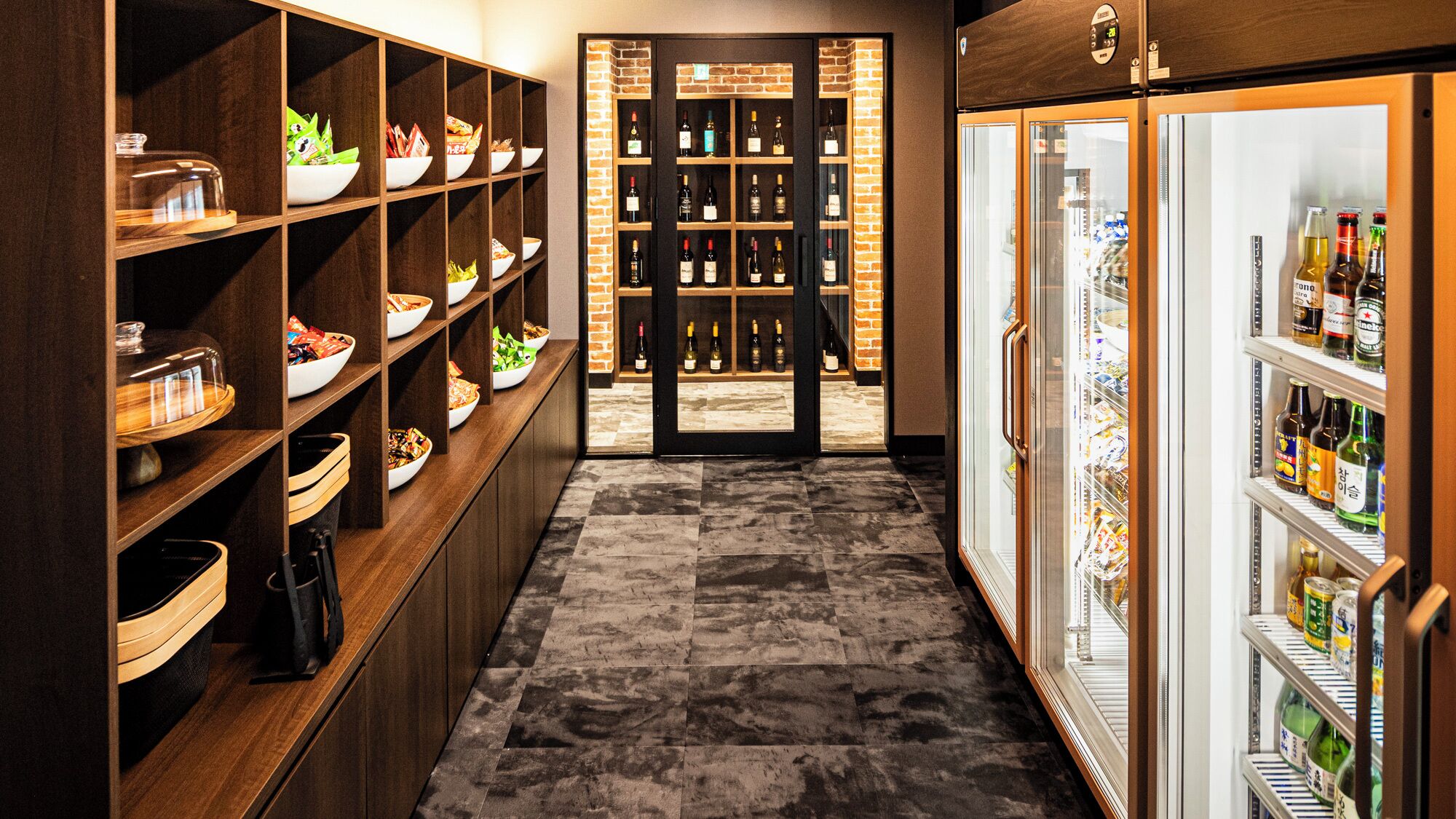 A corridor with wooden shelves on the left holding various food items and a wine cooler on the right.