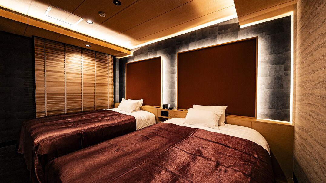 Habitación de hotel con dos camas, un ventanal grande con persianas y un diseño moderno que incorpora elementos de madera y piedra.