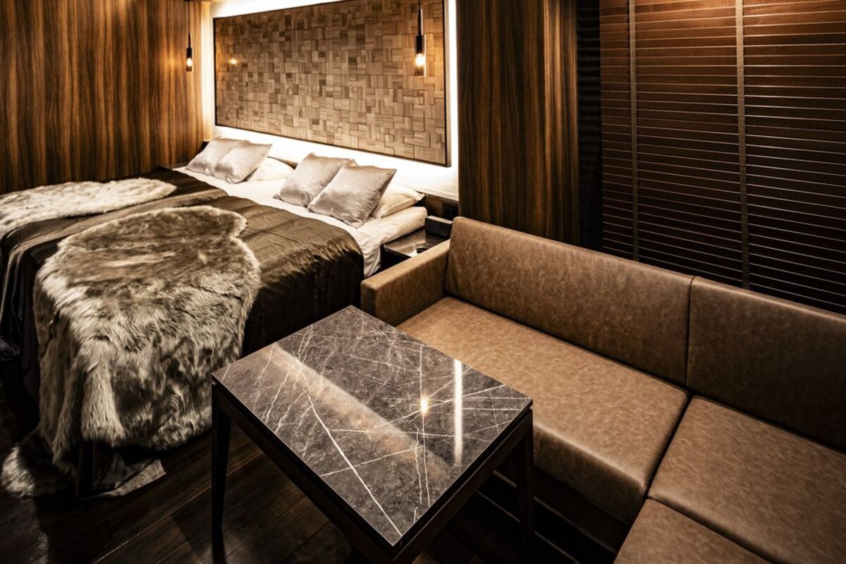 A room with a bed, a sofa, a marble table, and wooden paneling.