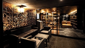 Un espacio lounge moderno con diseño geométrico en la pared, diferentes disposiciones de asientos y una barra visible.