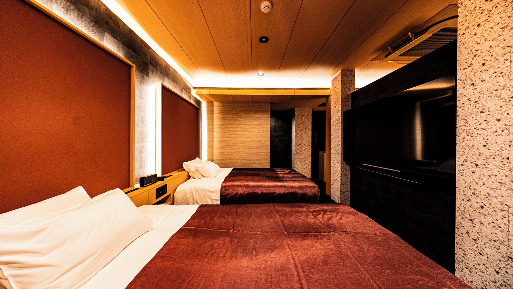 Quarto de hotel com duas camas, uma televisão e teto de madeira.