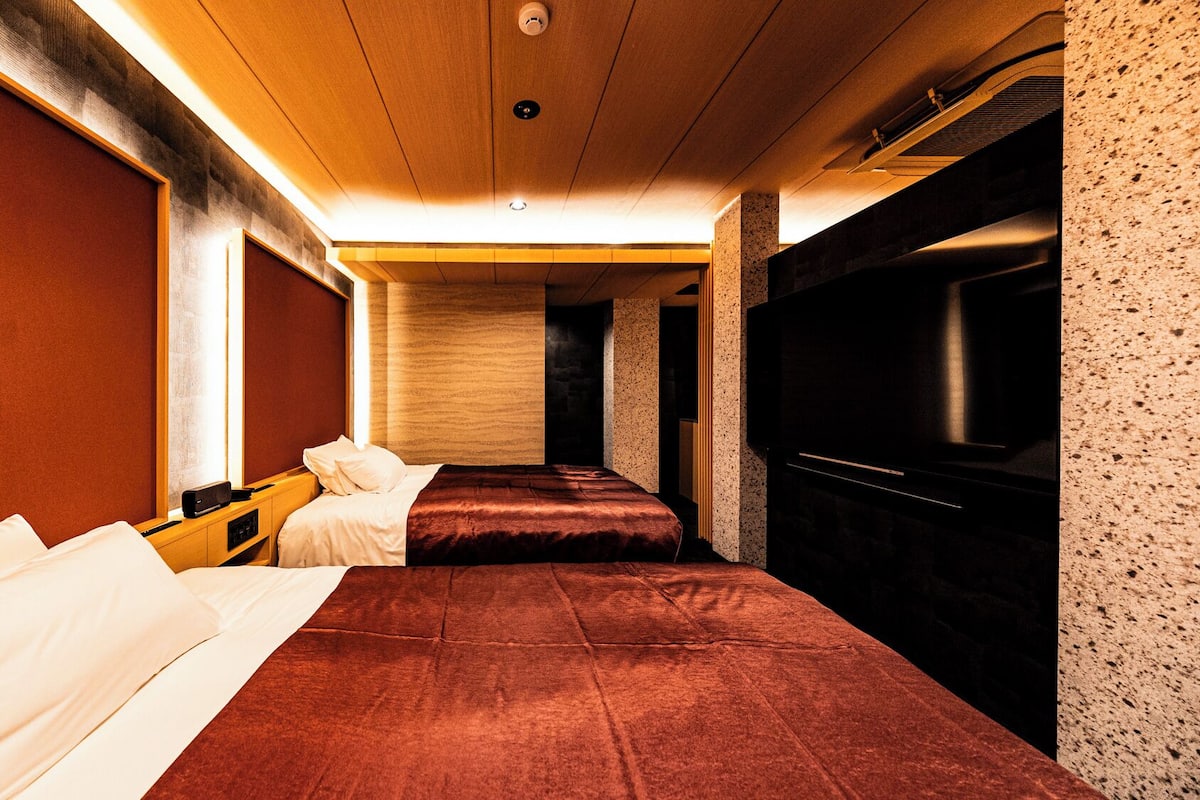 A hotel room with two beds, a TV, and a wooden ceiling.