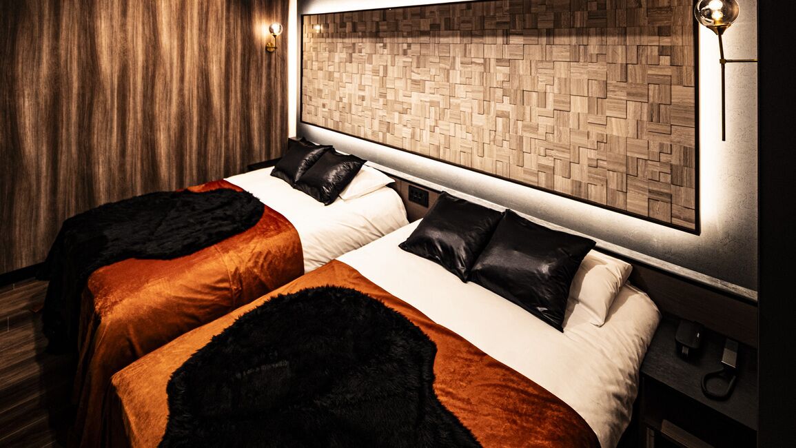 Habitación de hotel con dos camas, cabecero de madera, lámpara de pared y piso de madera.
