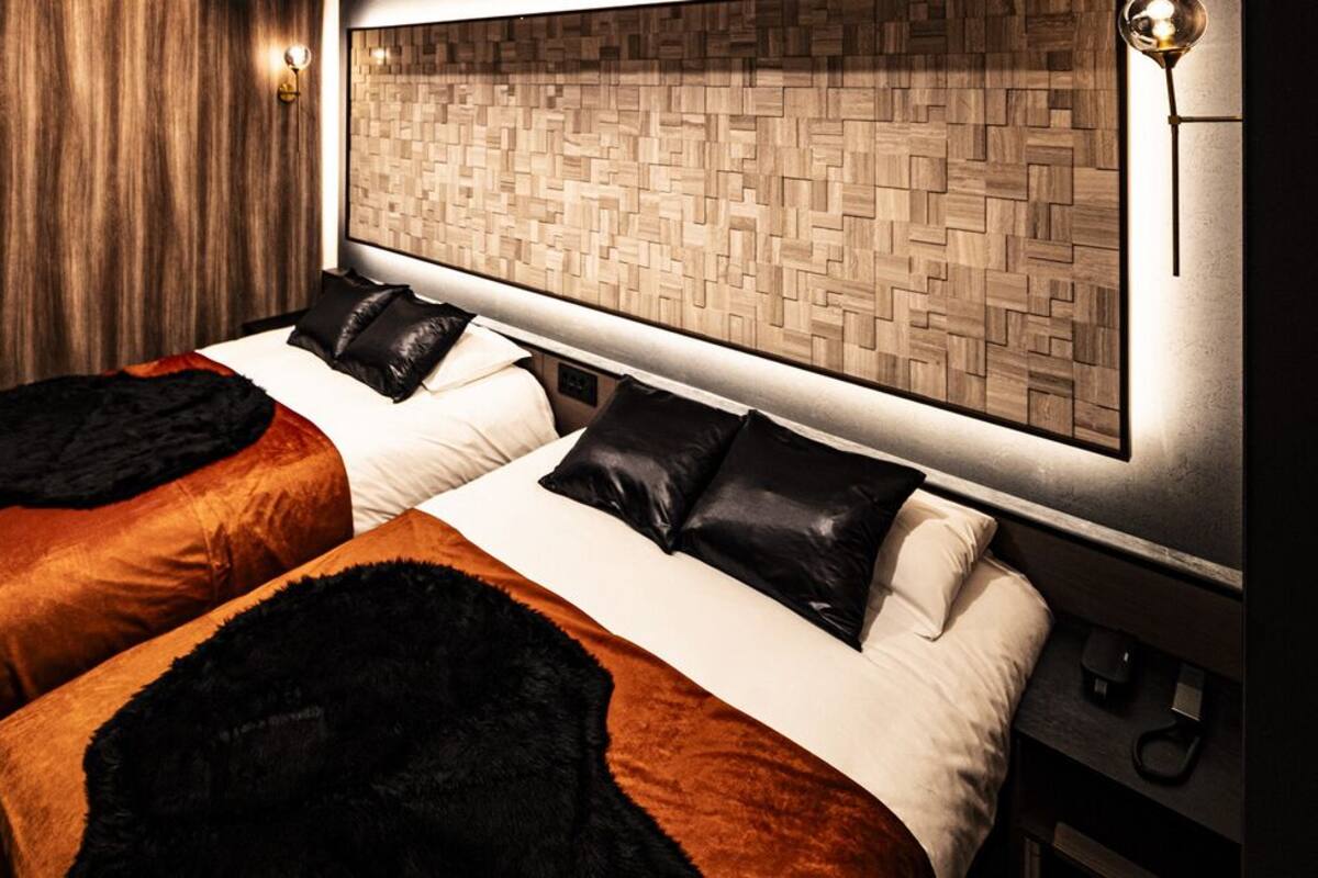 Habitación de hotel con dos camas, cabecero de madera, lámpara de pared y piso de madera.