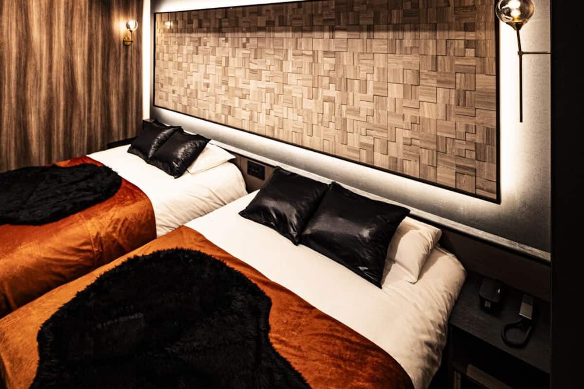 Habitación de hotel con dos camas, cabecero de madera, lámpara de pared y piso de madera.
