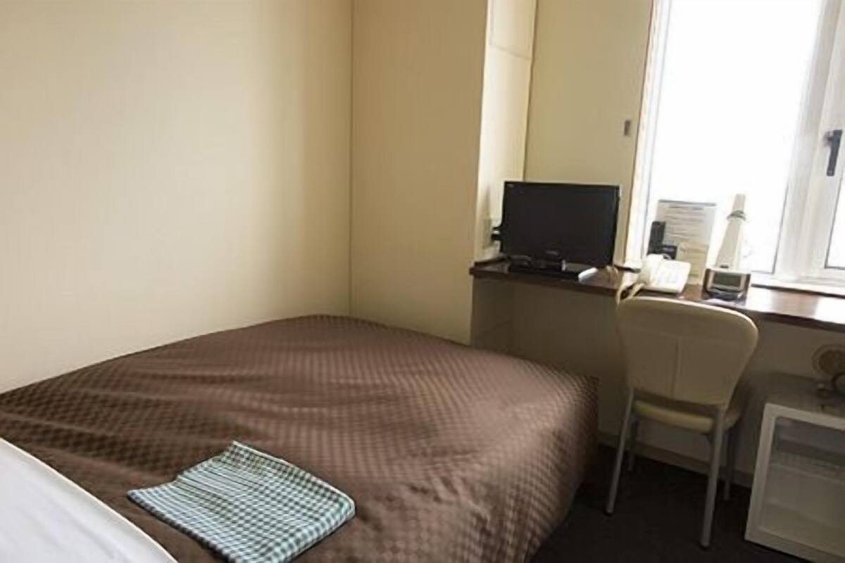 Ein Hotelzimmer mit Bett, Schreibtisch, Sessel, Fernseher und Fenster.