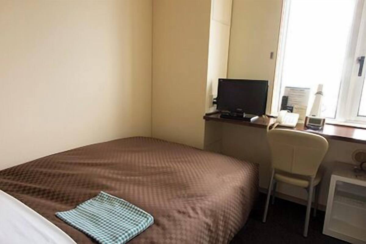 Ein Hotelzimmer mit einem Bett, einem Schreibtisch mit Computer, einem Stuhl und einem Fenster.