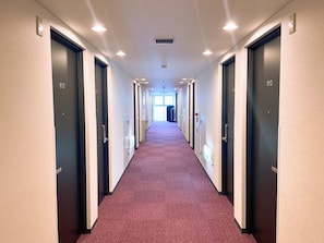 Corredor de hotel com portas numeradas 613 e 612, piso carpete e iluminação embutida no teto.