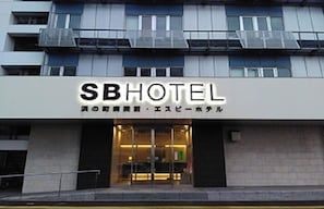 Entrada de hotel com uma placa indicando 'SBHOTEL' e texto em japonês abaixo.