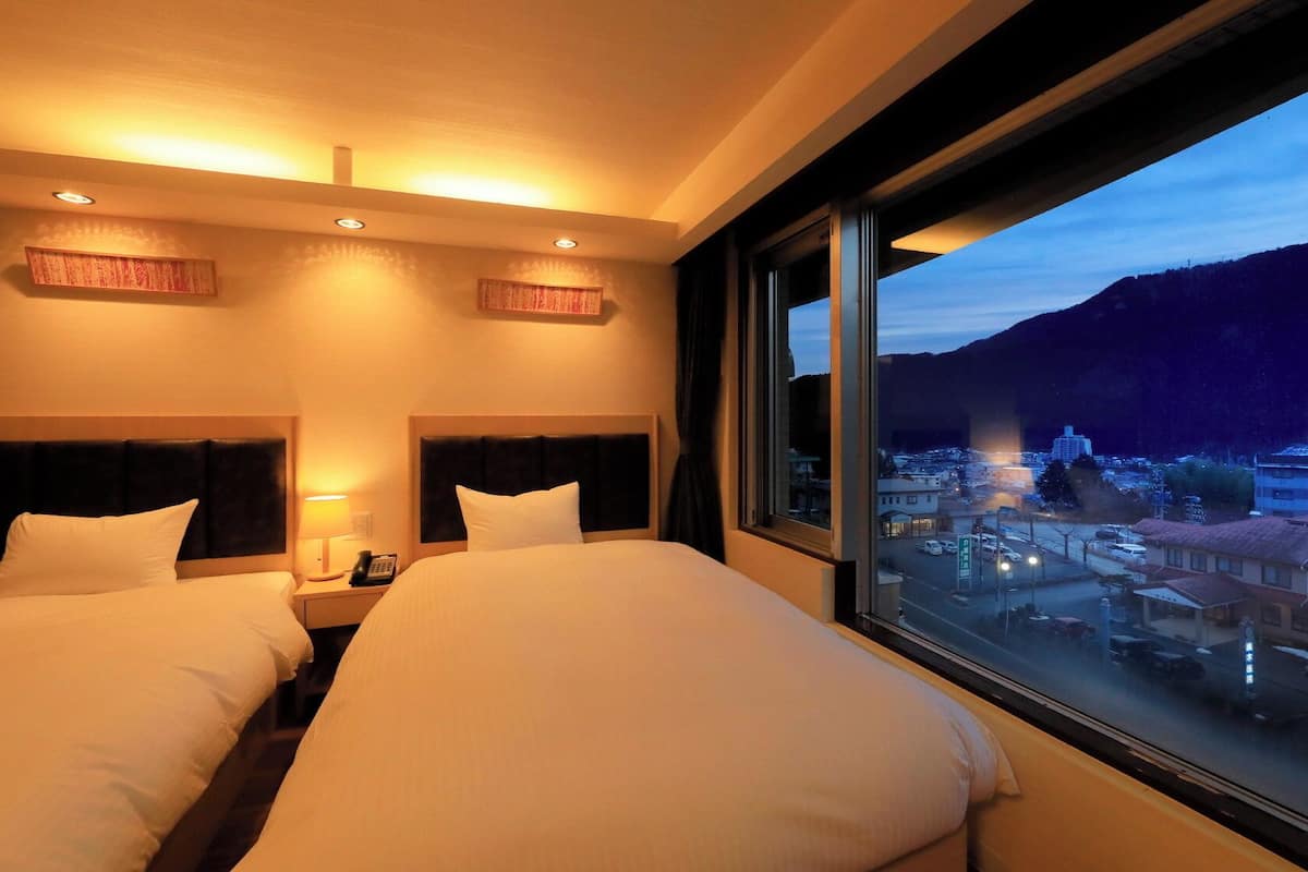 A hotel room with two beds, a large window, and a view of a cityscape.