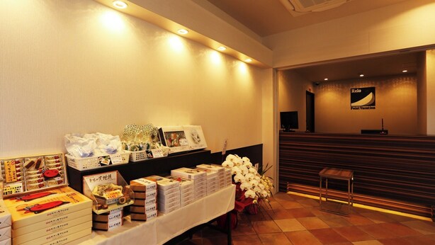 A reception area with a reception desk, a wall-mounted sign, and a table with various food items and boxes. - Point Vacation Gero (Gero)