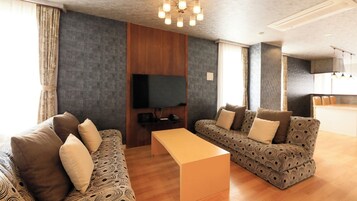 Una sala de estar moderna con un juego de sofá, una mesa de centro, un televisor de pantalla plana y una cocina al fondo.