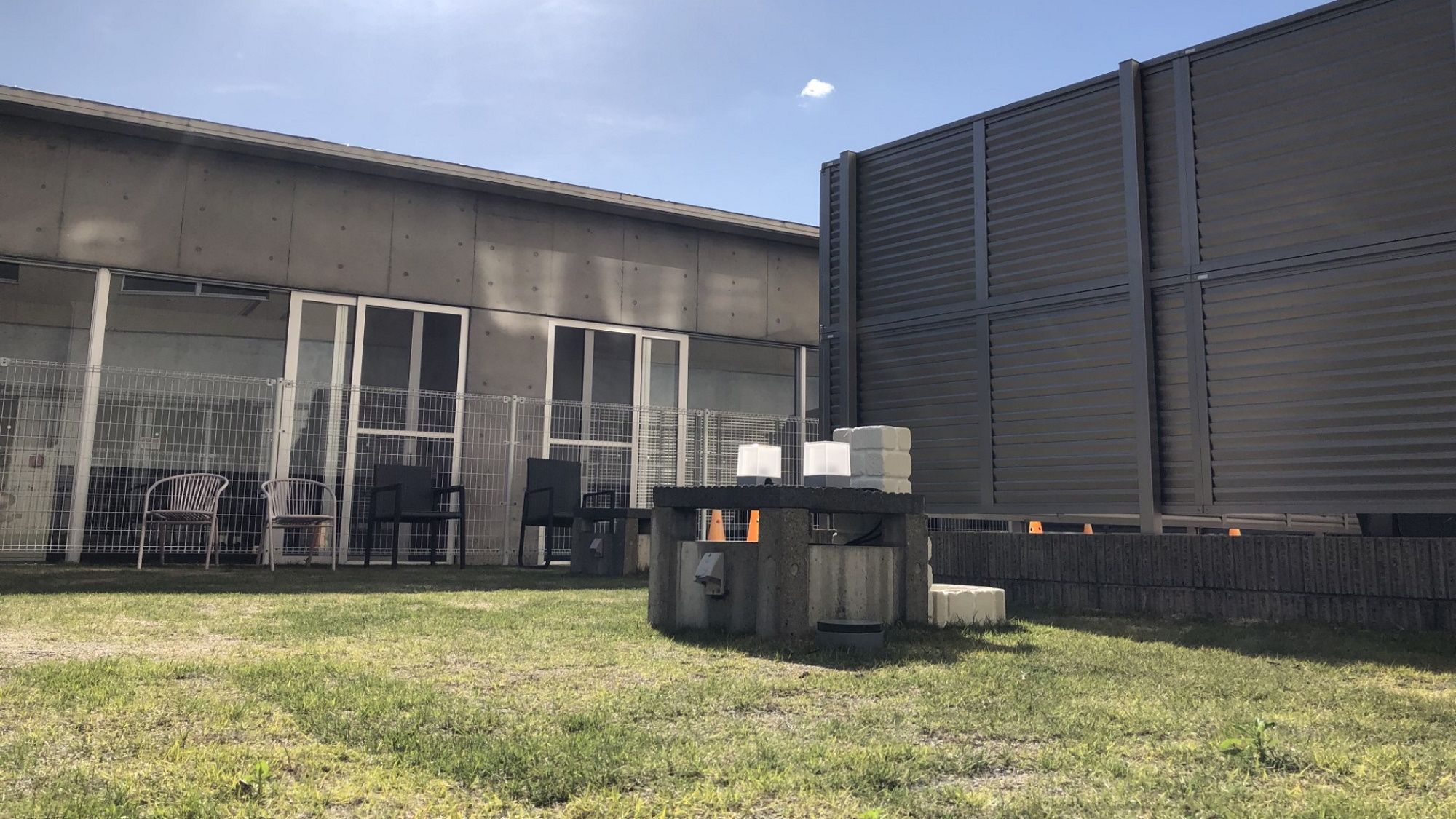 A fenced outdoor area with a building, chairs, and a trash bin.