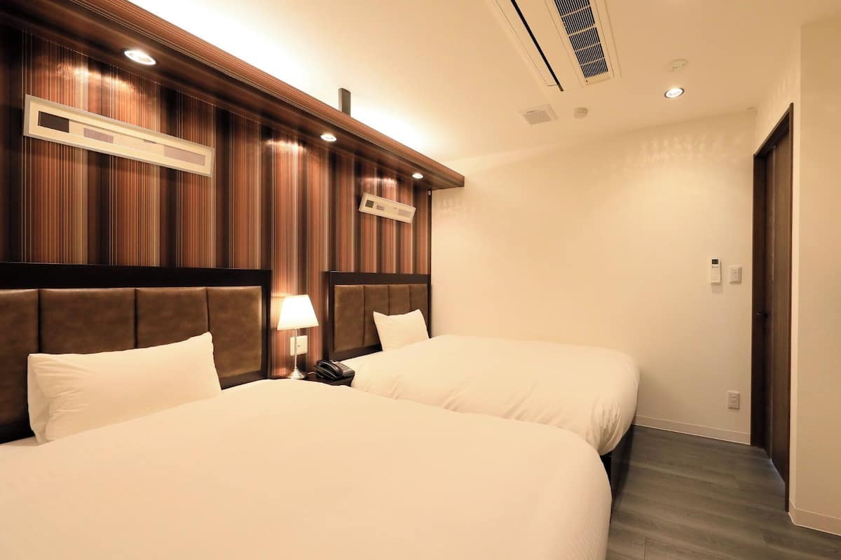 A hotel room with two beds, a TV, a phone, and a lamp.