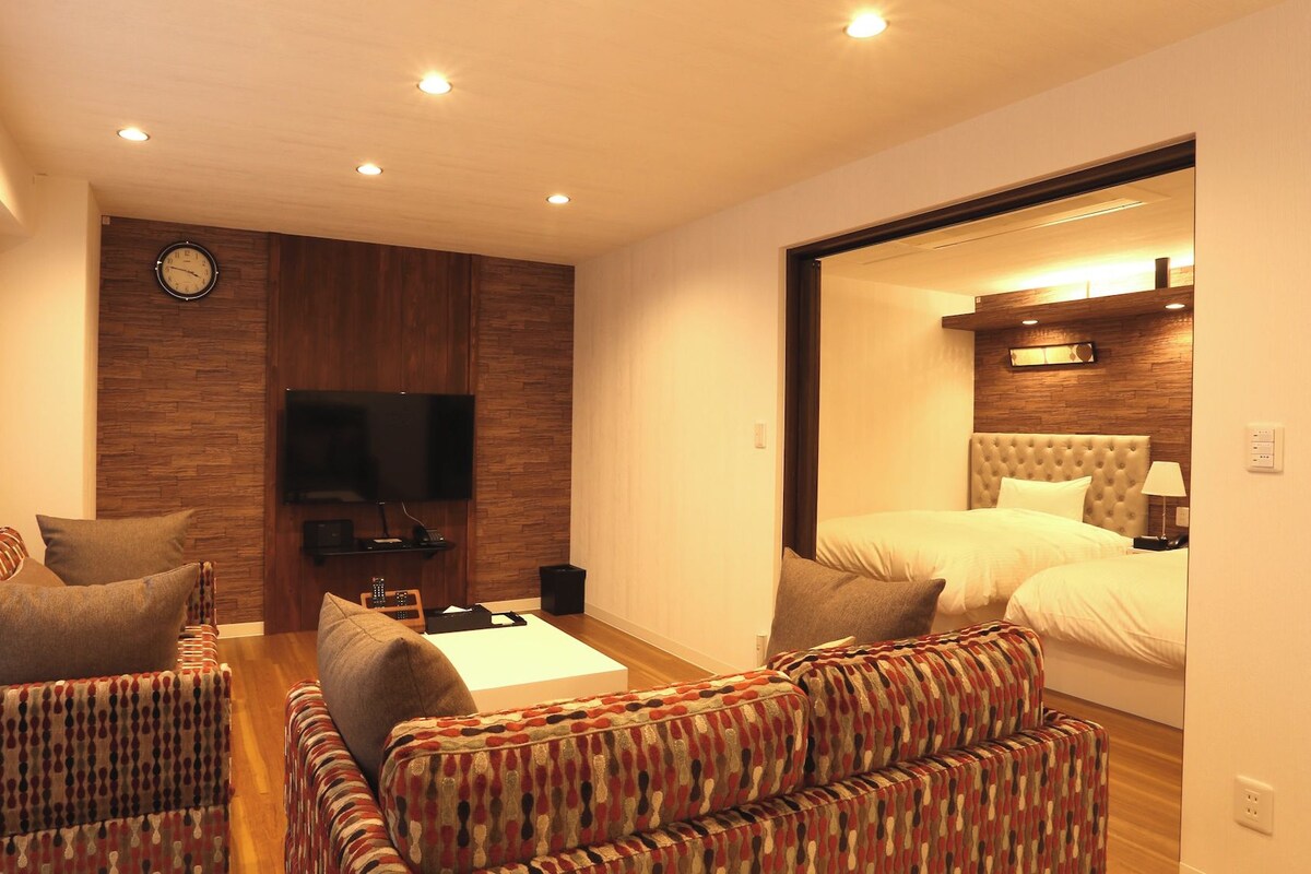 Habitación de hotel con un sofá, una cama, un televisor y una pared decorativa de madera.
