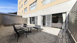 Ein Gebäude mit einer Terrassenfläche, die einen Tisch und Stühle sowie eine überdachte Sitzgruppe bietet und einen Blick ins Innere durch Glastüren gewährt.