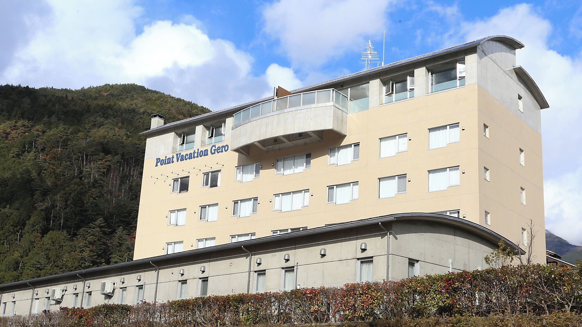 A multi-story hotel with a balcony on the upper floor, surrounded by a mountainous landscape.