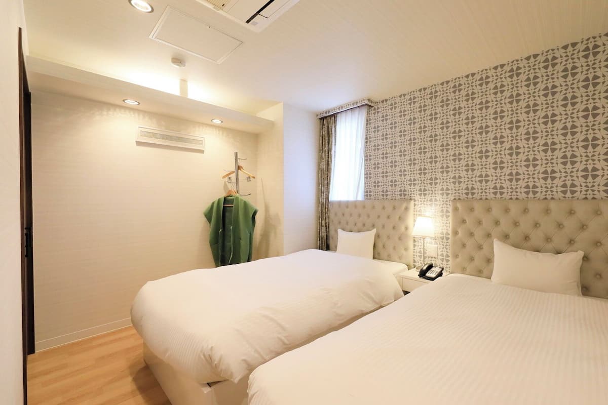 A hotel room with two beds, a patterned headboard, a hanging coat rack, and a bedside telephone.
