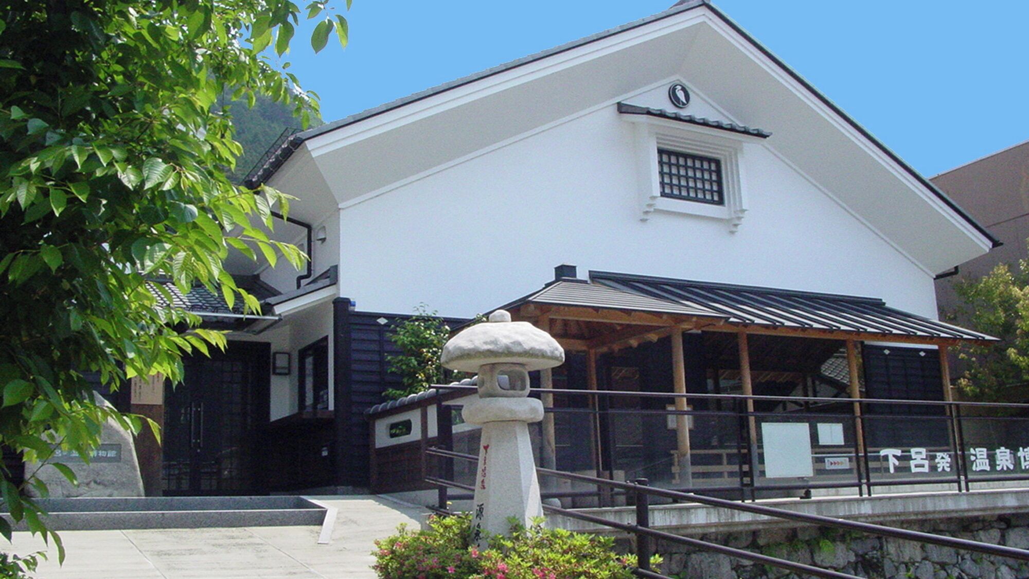 A traditional Japanese building with a white facade, a black roof, and a stone lantern in the foreground.
