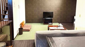 A hotel room with a TV on a stand, a sofa, a small table, a trash bin, and a staircase. - Green House Goryokaku (Hakodate)
