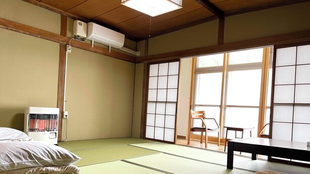 A tatami mat room with a futon bed, a heater, sliding shoji doors, and a view through the windows. - Green House Goryokaku (Hakodate)