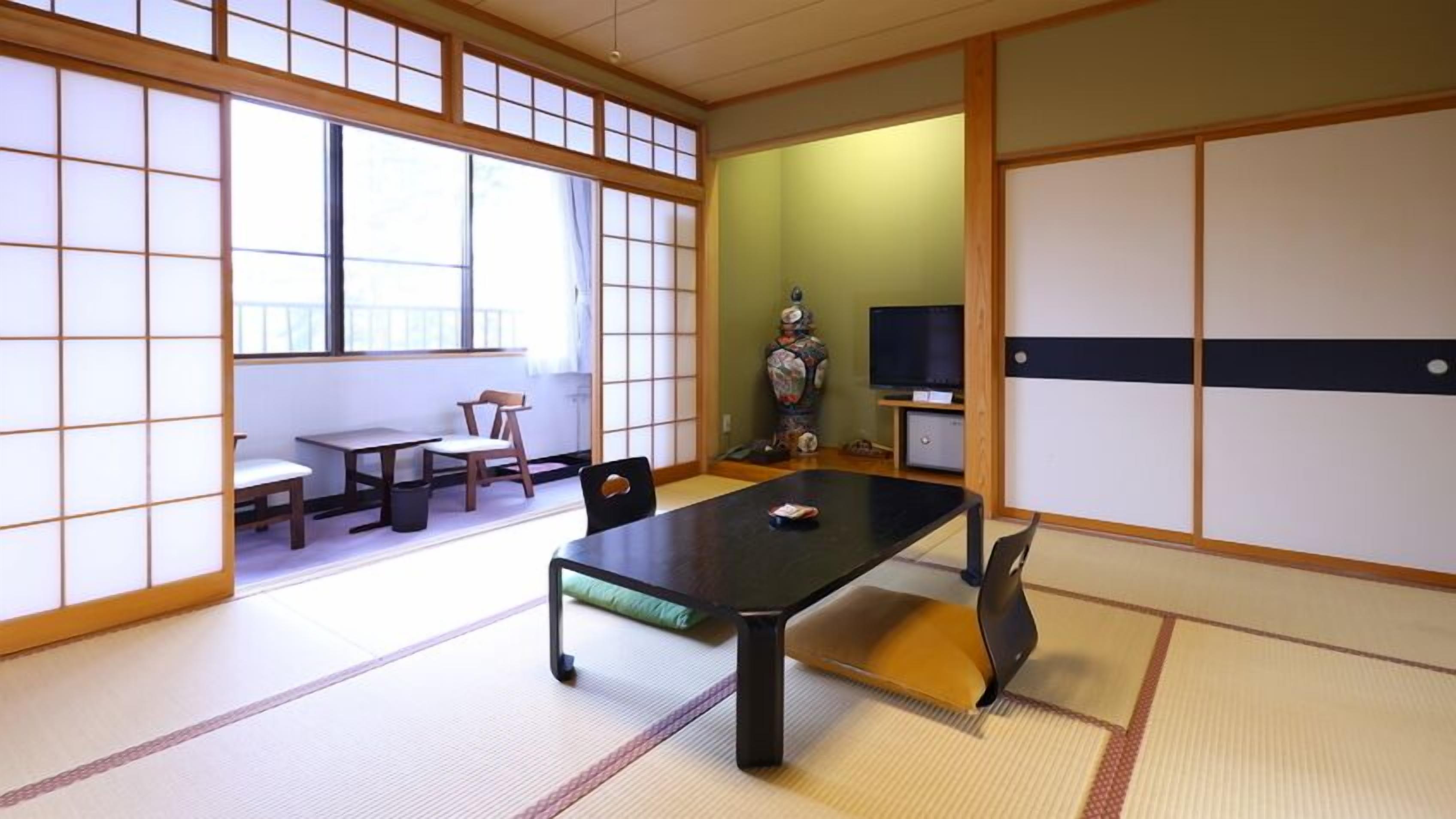 A traditional Japanese room with tatami flooring, a low table, chairs, a television, and a decorative vase.