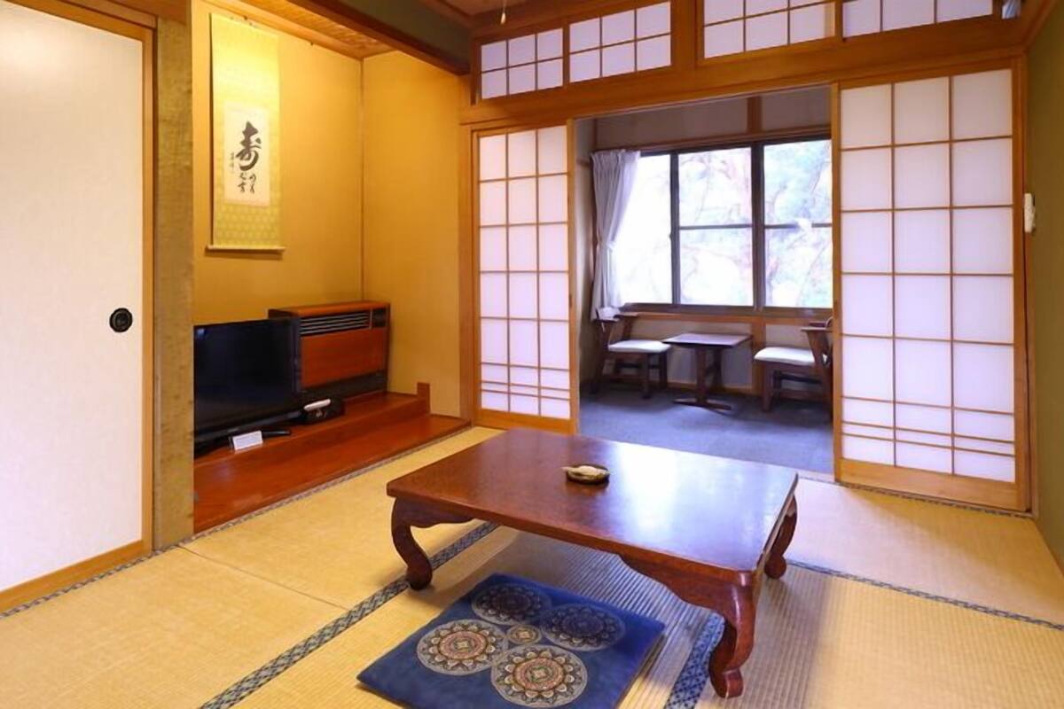 Ein traditioneller japanischer Raum mit Tatami-Bodenbelag, einem niedrigen Holztisch, einem Fernseher und gleitenden Shoji-Schiebetüren.