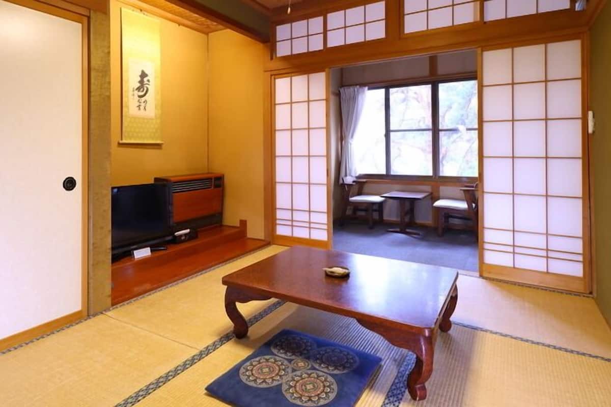 A traditional Japanese room with tatami flooring, a low wooden table, a television, and sliding shoji doors.