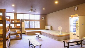 A room with a wooden bench, a small table, a vending machine, and a window with a view of trees. - Azumino Hotaka Onsenkyo Ryokan Yama no Takohei (Azumino)