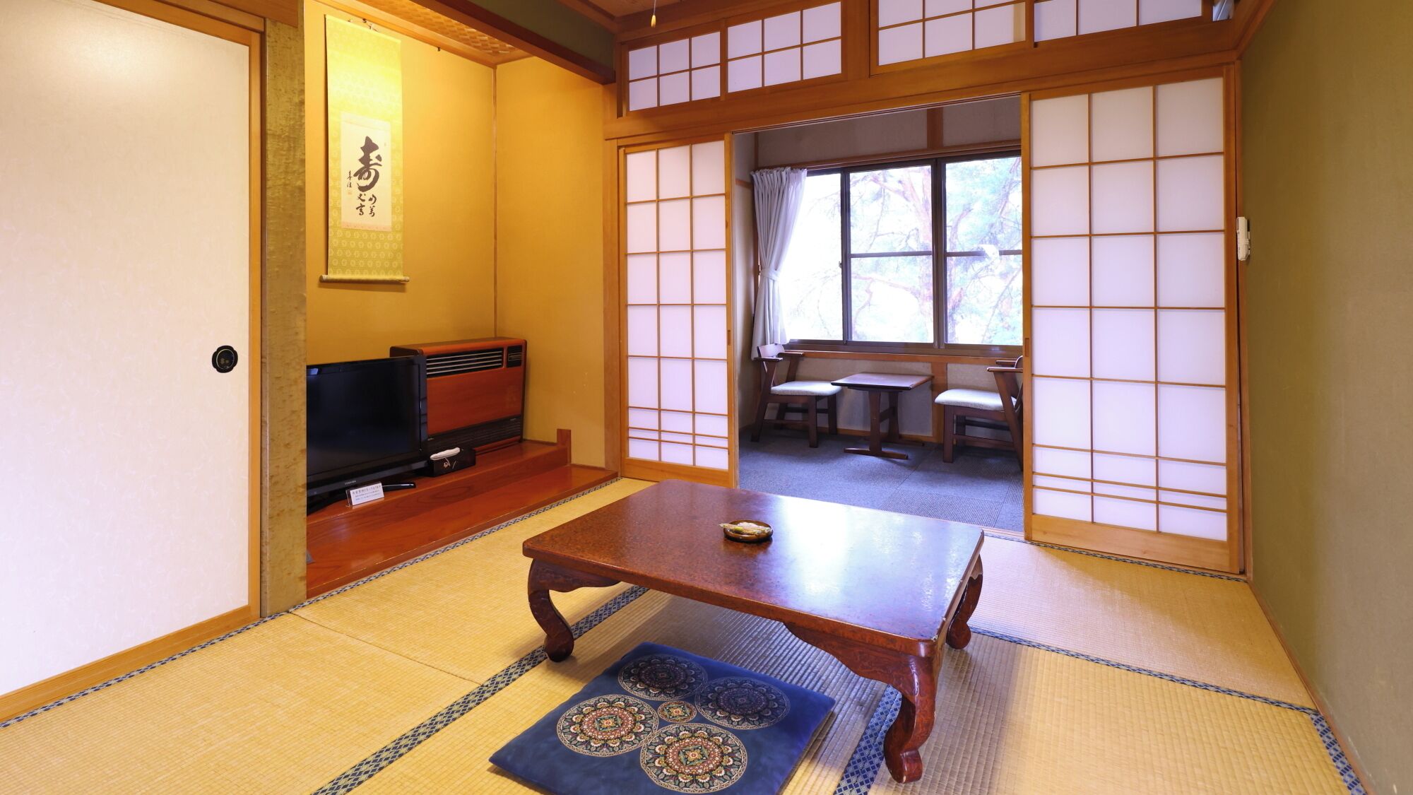 A traditional Japanese room with tatami flooring, a low table, a television, and sliding doors leading to a dining area.
