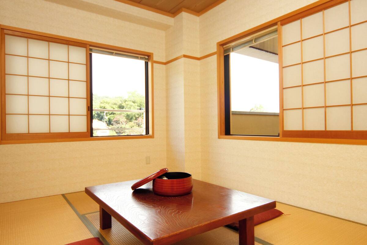 A traditional Japanese room with tatami flooring, shoji screens, and a low wooden table with a red container.
