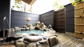 A stone hot tub surrounded by rocks, a wooden gate, and a bamboo fence. - Shofuso (Miyazu)