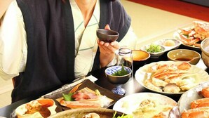 A person seated at a table with various dishes, including seafood and vegetables, in a room with a simple layout. - Shofuso (Miyazu)