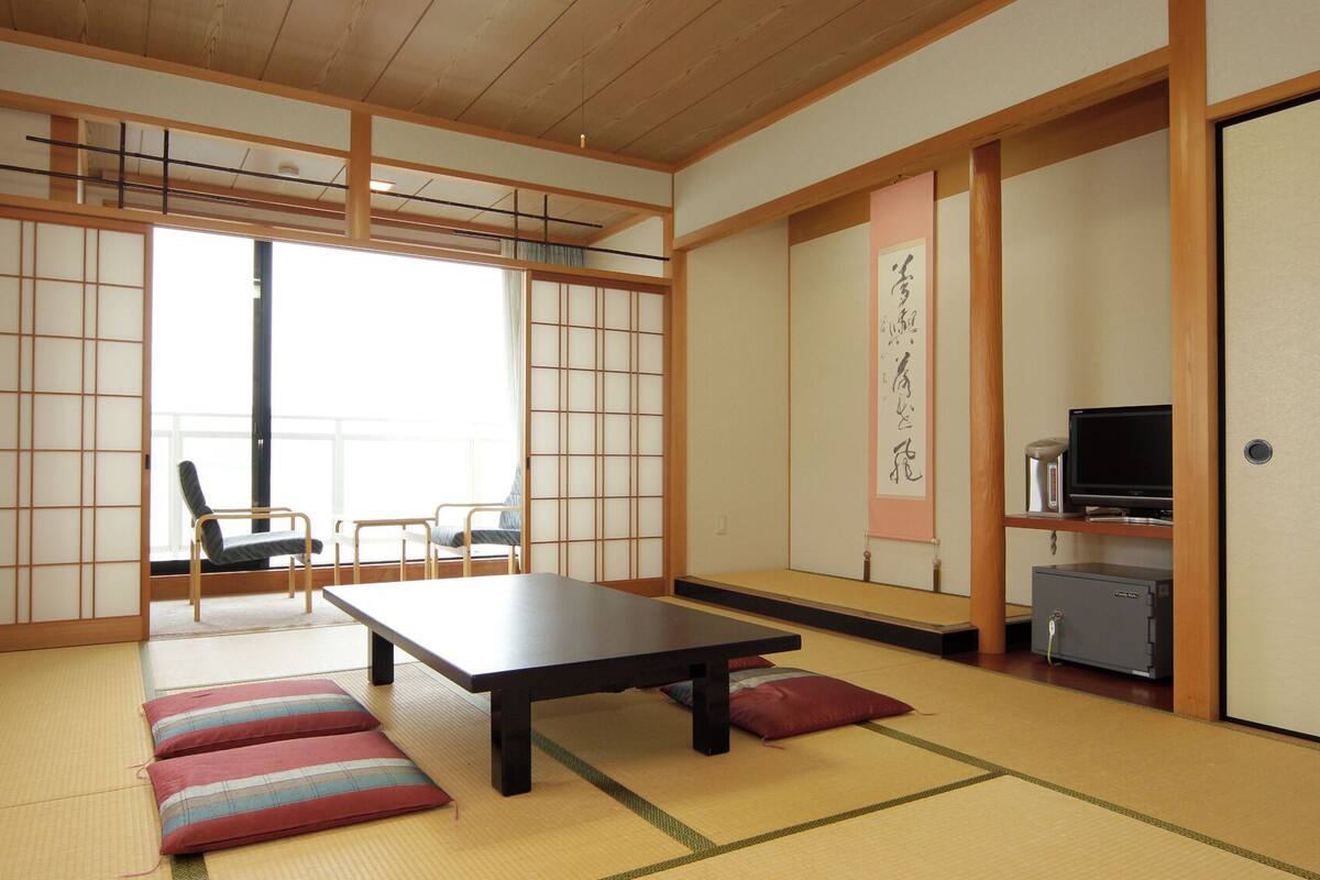 A traditional Japanese room with tatami flooring, a low table, a sofa, and a television.