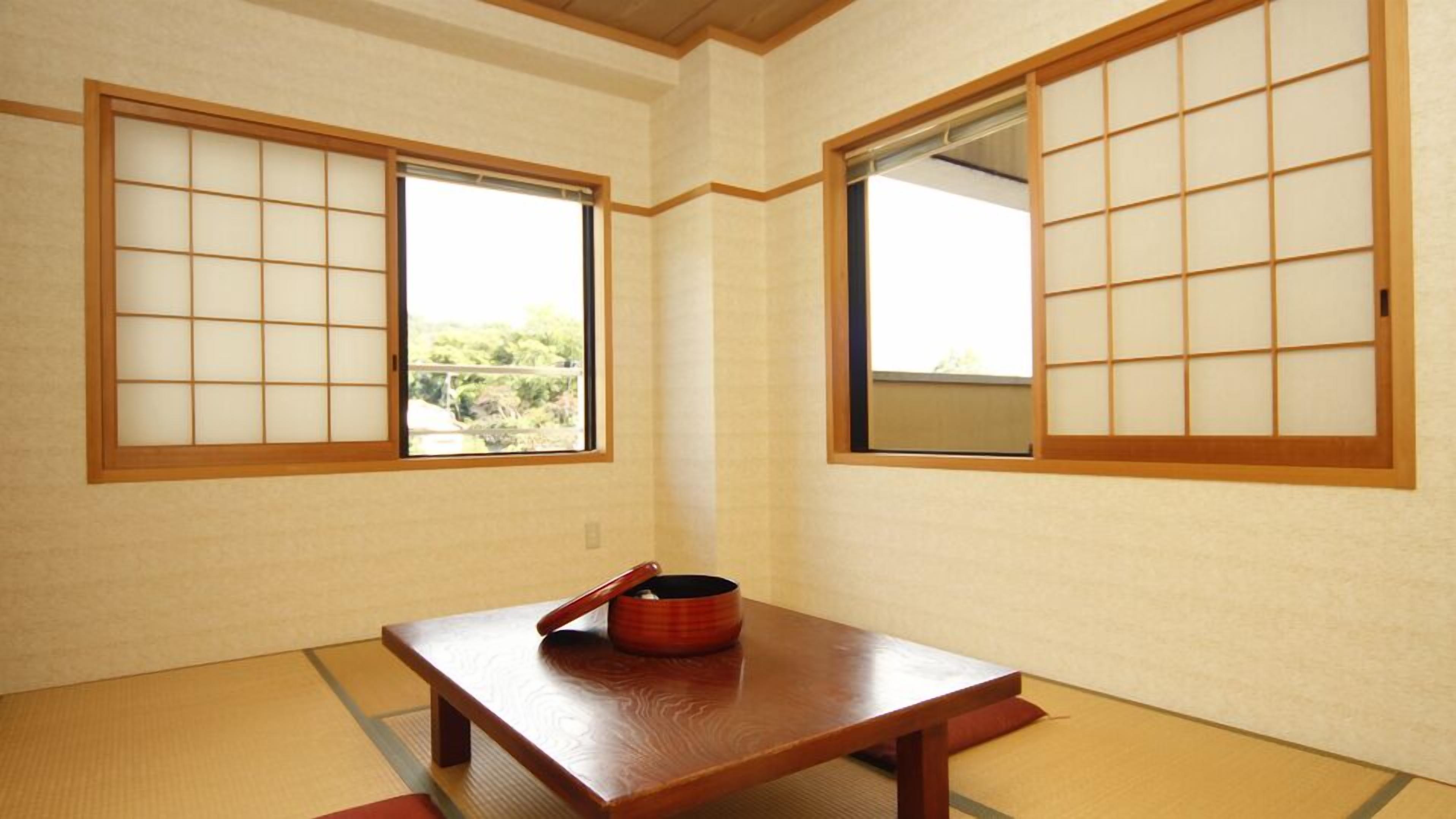 Una habitación japonesa tradicional con suelo de tatami, paneles shoji y una mesa de madera baja con un recipiente rojo.