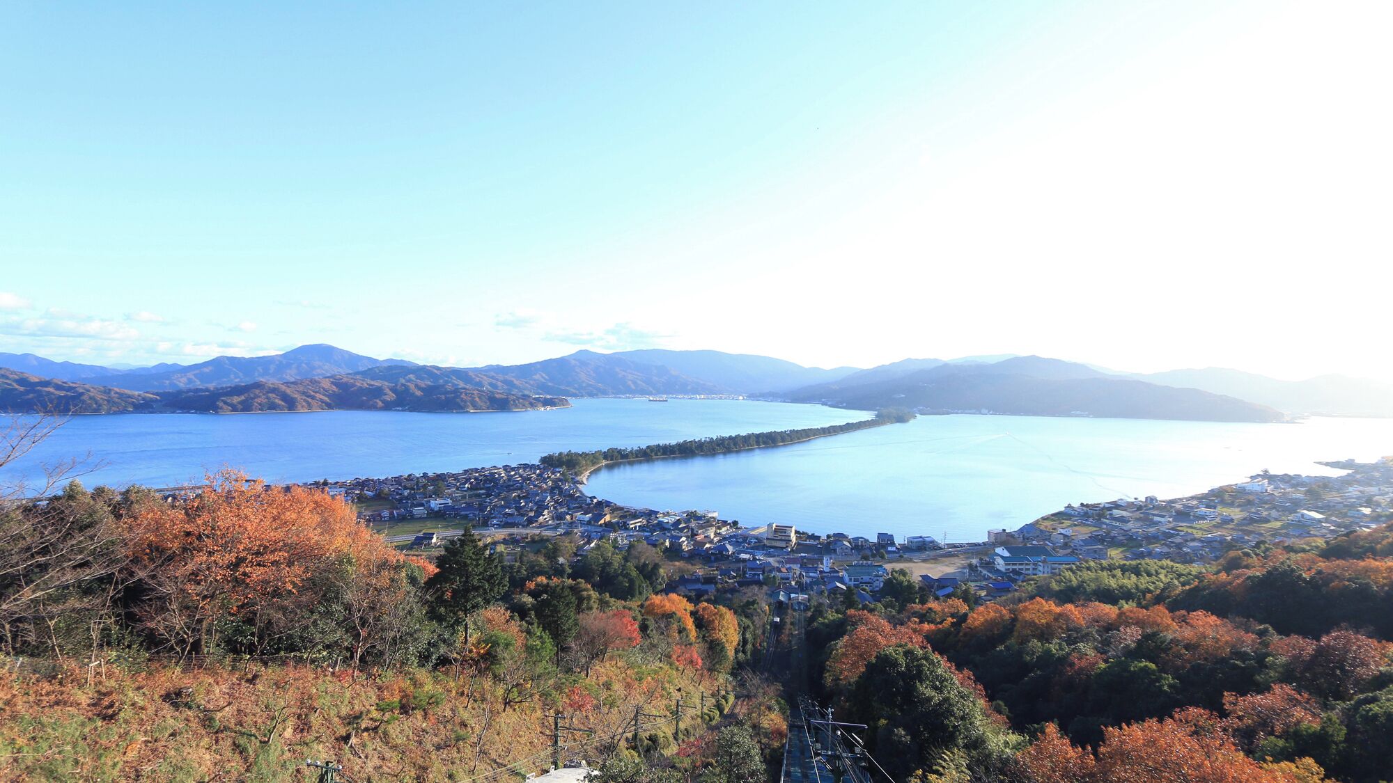 A coastal town with a marina, autumn foliage, and mountains in the background.
