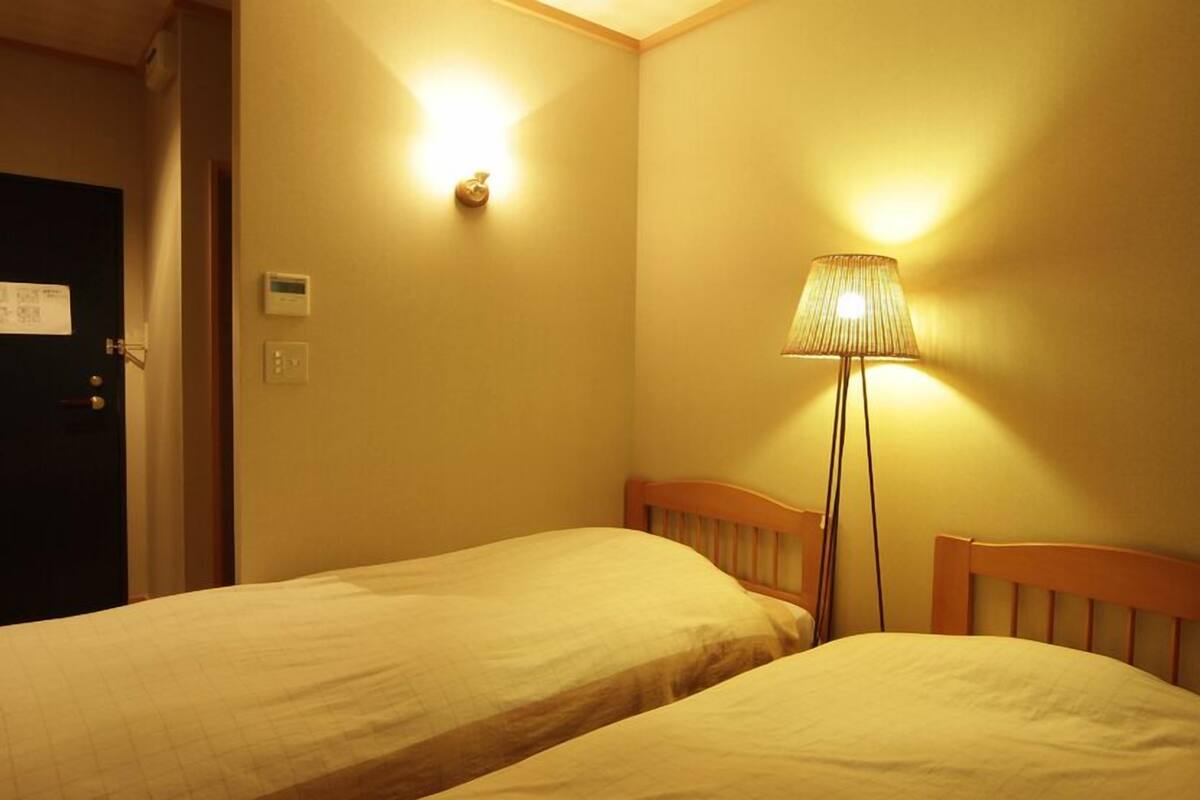 A hotel room with two single beds, a nightstand, a lamp, and a door.