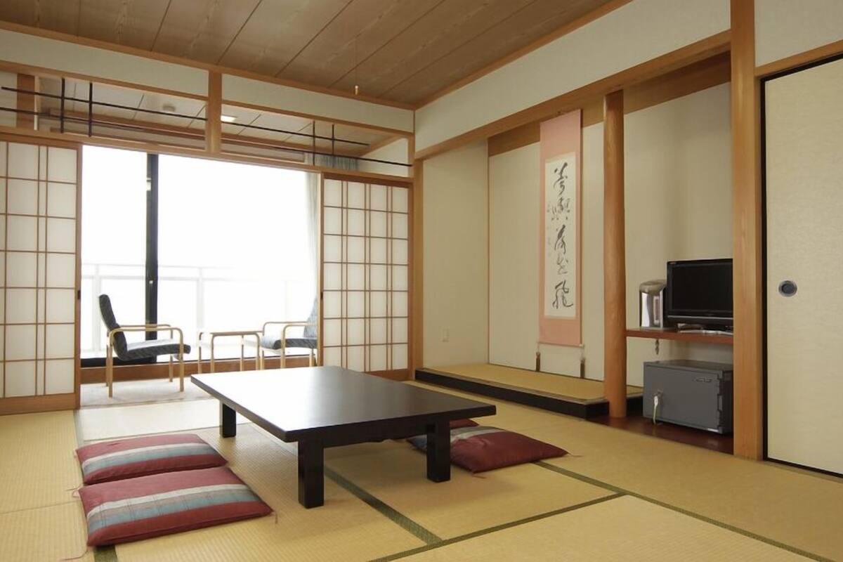 A traditional Japanese room with tatami flooring, a low table, cushions, a sliding door, and a television.