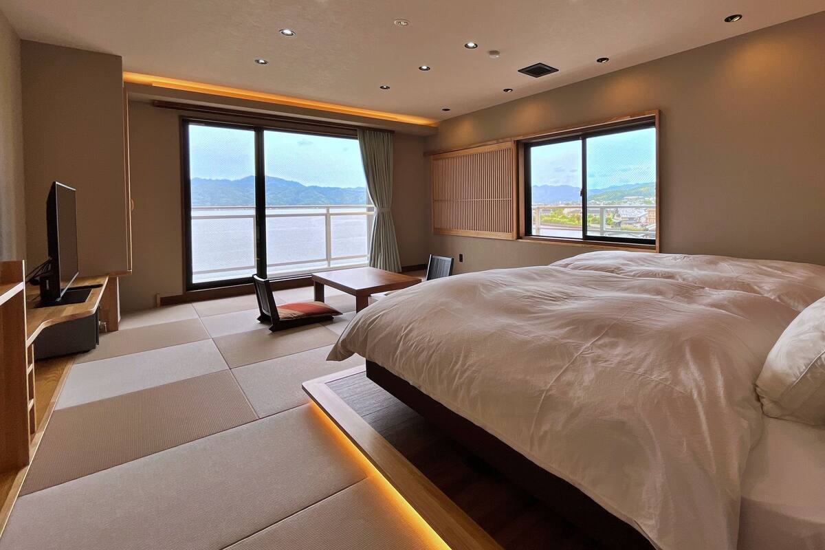 A modern hotel room with a large bed, a TV, a desk, and a view of the mountains.