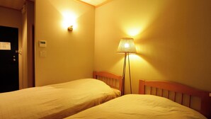 A hotel room with two single beds, a standing lamp, a door, and a wall-mounted light fixture. - Shofuso (Miyazu)