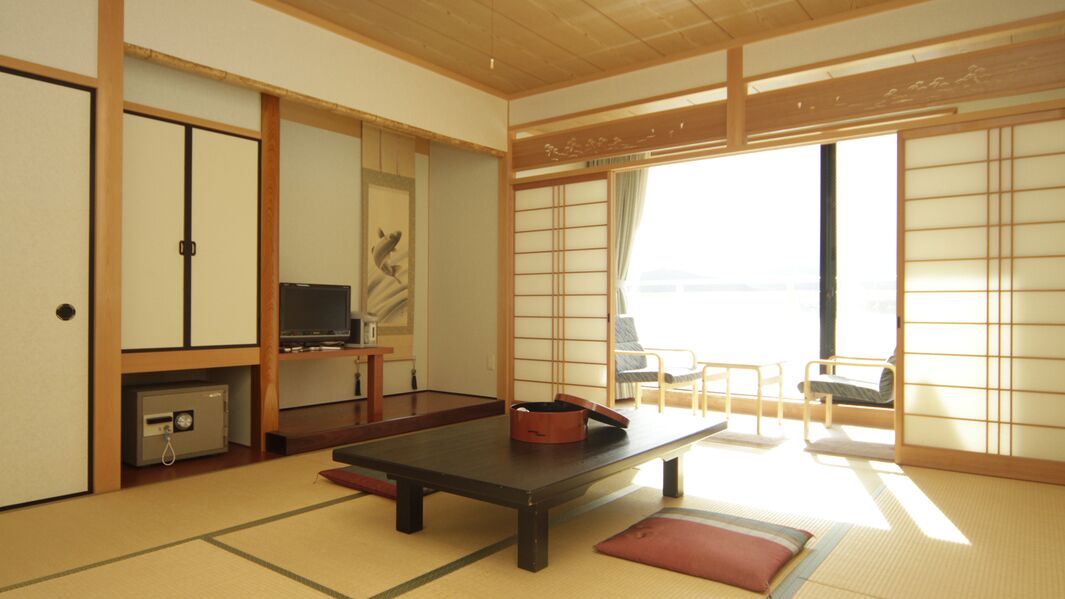 Una habitación japonesa tradicional con suelo de tatami, una mesita baja, televisor, puertas correderas y vistas por una ventana.